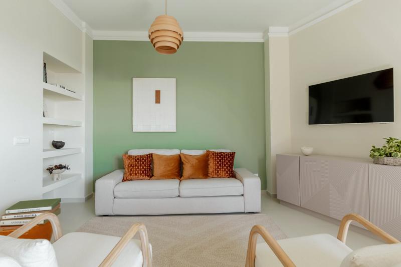 Wohnzimmer mit salbeigrüner Wand, Sofa mit terrakottafarbenen Kissen und zwei Sesseln