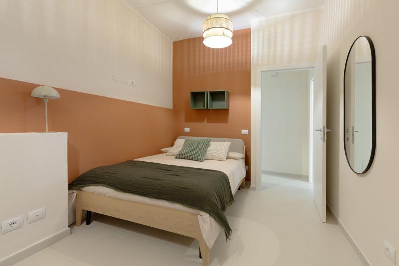 Schlafzimmer mit halb korallfarben gestrichener Wand, Holzbett und olivfarbener Decke